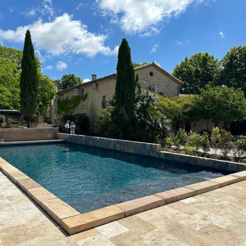 Cette image montre la nouvelle piscine du Mas des Violettes, un domaine viticole situé dans les Cévennes, à Valflaunes. La piscine est construite en pierre de taille, un matériau qui s'intègre parfaitement au cadre historique du domaine. La membrane armée Renolit 3D Touch Élégance offre un aspect moderne et élégant à la piscine.